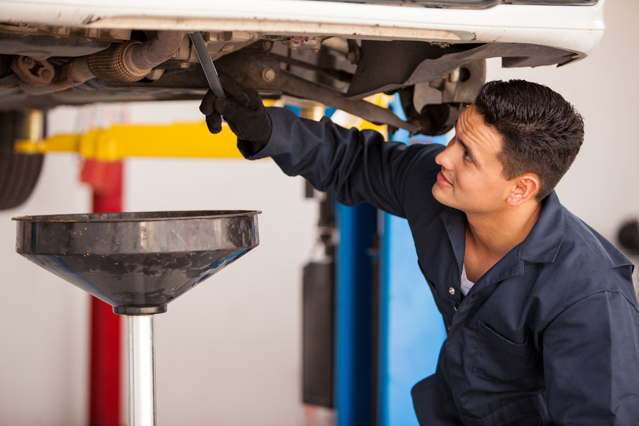 Young Hispanic mechanic draining engine oil from a car for an oil change at an auto shop